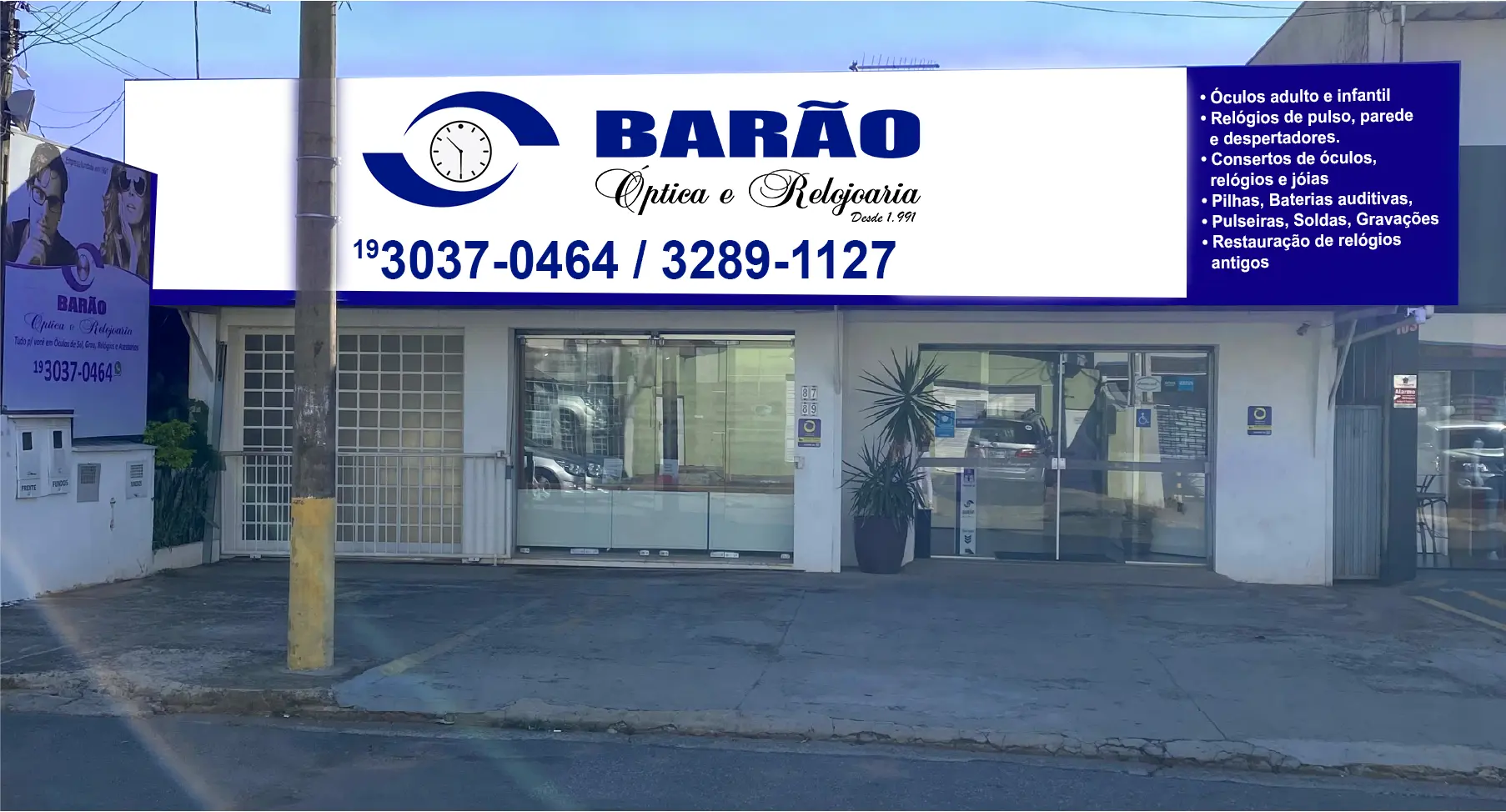 Fachada da Óptica Barão com letreiro azul e branco e entrada da loja
